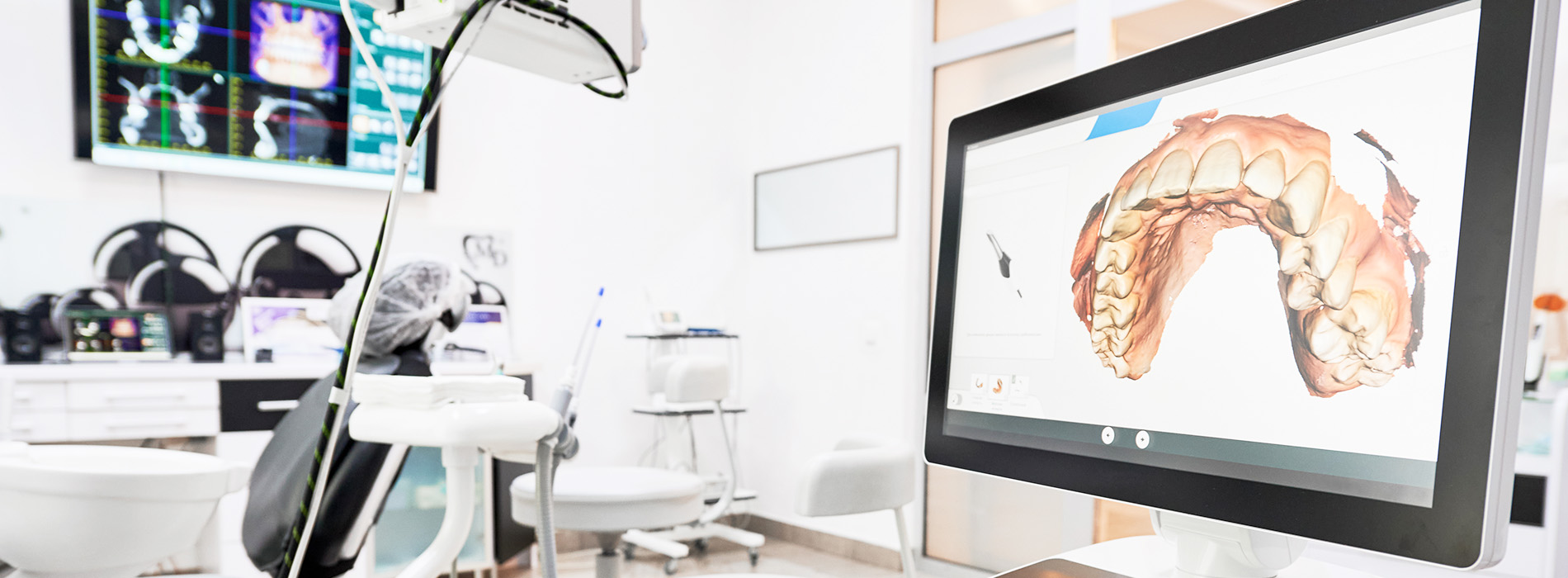 An image showing a modern dental office with a computer monitor displaying an animated toothbrush, a dental chair, and various pieces of dental equipment.