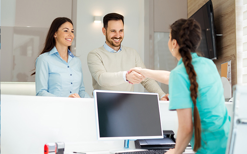The image shows three individuals in an office environment  a man and woman shaking hands with another person who appears to be receiving the handshake, suggesting a formal greeting or agreement being made.