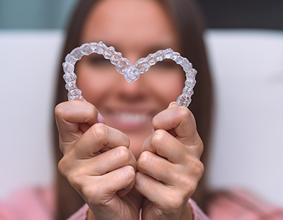 A person holding up a heart-shaped dental appliance with both hands against a blurred background.