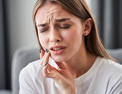 A young woman with her eyes closed, holding her face with both hands, seemingly experiencing discomfort or pain, possibly indicating a dental issue such as an abscess or severe toothache.