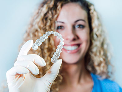 A woman wearing a surgical mask holds up a transparent dental implant with a smile.