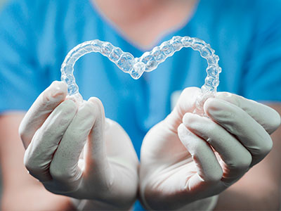 An alternative text description for an image featuring a medical professional holding a heart-shaped object made from clear dental material, symbolizing dental health and care.