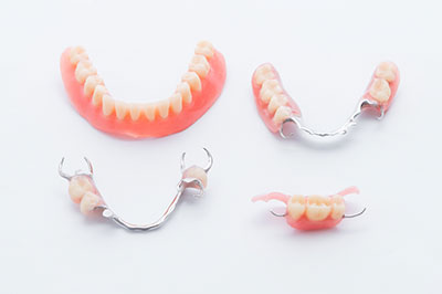 The image displays a set of dentures with visible teeth on a white background, alongside two pairs of metal dental braces.