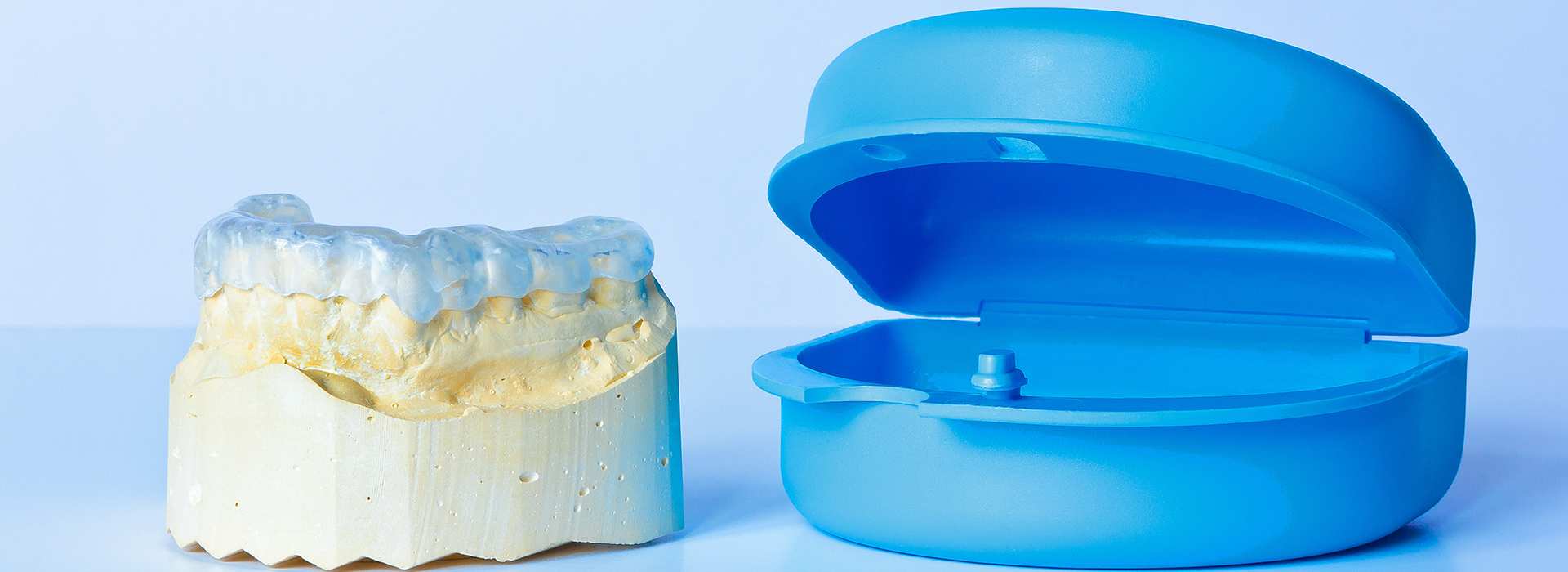 The image shows a transparent blue plastic container next to a yellow object with a hole in the center, which appears to be a dental implant model or a wax-up for a dental restoration.