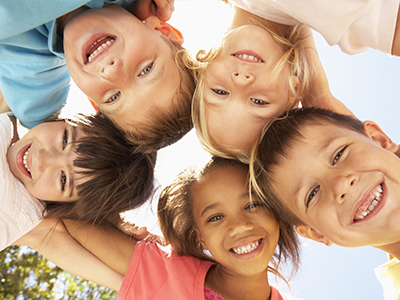 The image depicts a group of children of various ages and genders, smiling and posing together for a photo with their arms around each other s shoulders.