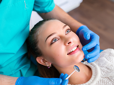 A dental hygienist is performing a teeth cleaning procedure on a seated patient with blue eyes.