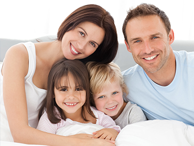 A family of four posing together on a bed with smiles on their faces.